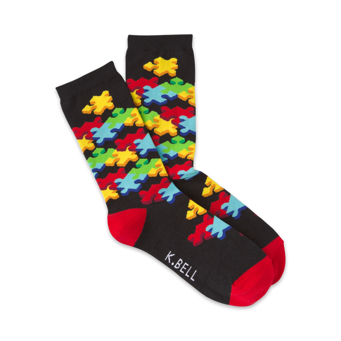 Pair of crew socks on a white background.  The socks are black with a colorful jigsaw puzzle design and red cuffs.