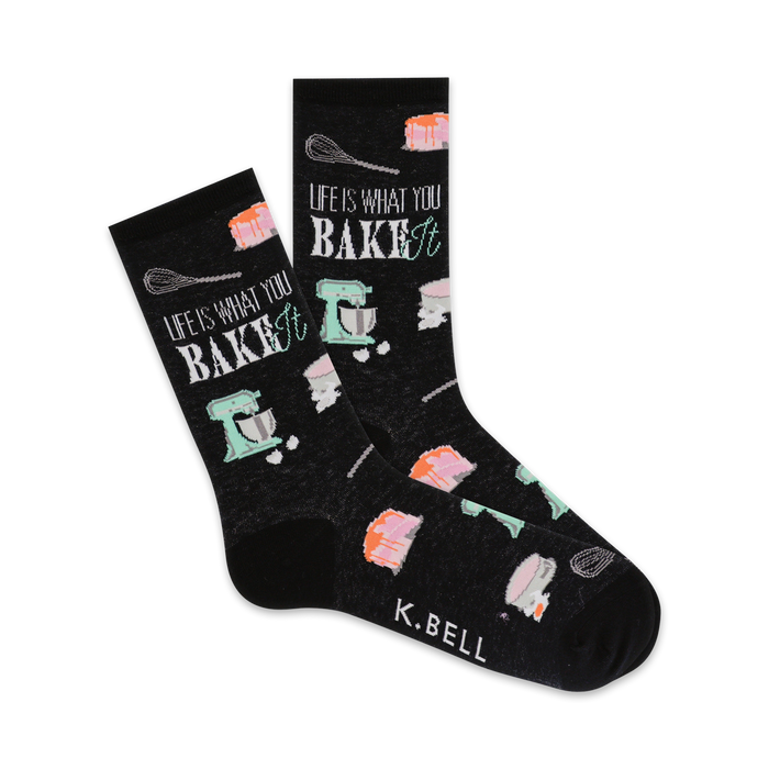 A pair of black crew socks with a baking-themed design. The socks feature pastel-colored images of cakes, whisks, and stand mixers, along with the text 'Life is what you bake it'. }}
