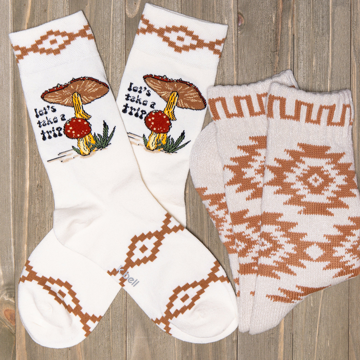 Flat lay showcasing 'Let's Take a Trip' crew socks and a pair of coordinating ankle socks with southwestern pattern on a wood background.