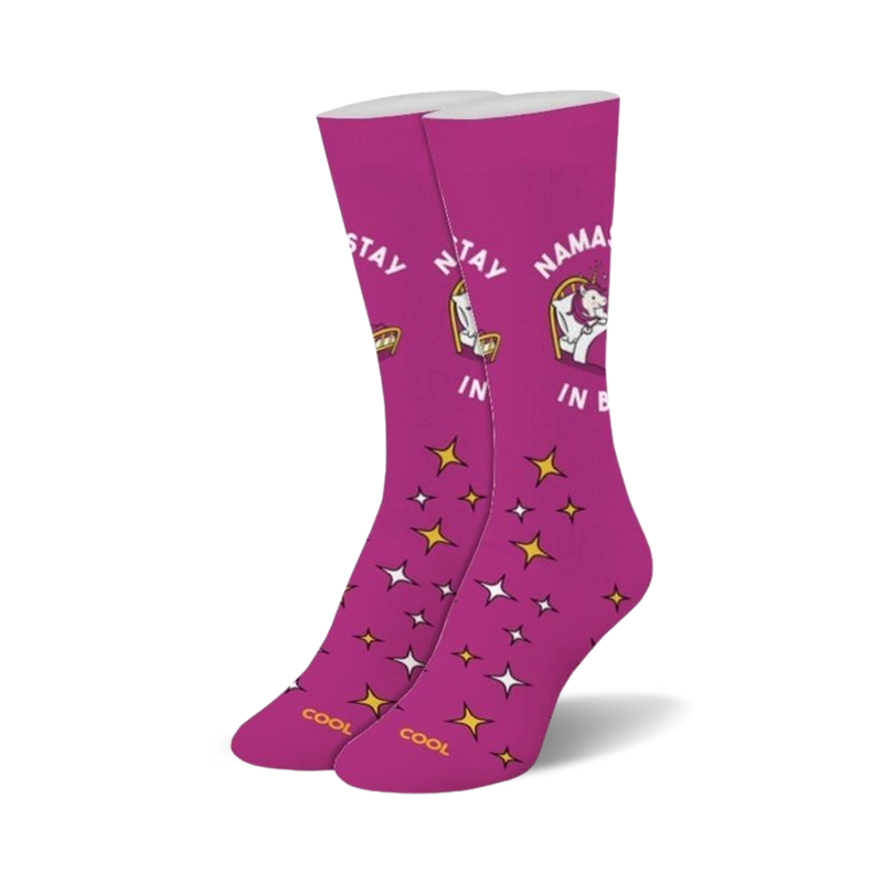 Pair of magenta crew socks with a whimsical unicorn design, gold stars, and the text 'Namastay In Bed'.