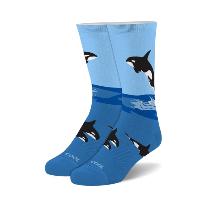 A pair of blue crew socks with a playful design featuring black and white orcas leaping from the ocean waves. }}