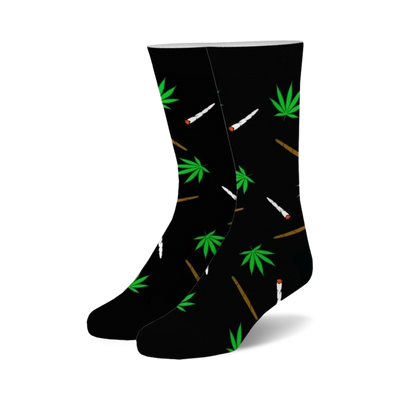 Pair of black crew socks with a whimsical design. Green marijuana leaves and stylized joints are scattered across the black fabric.