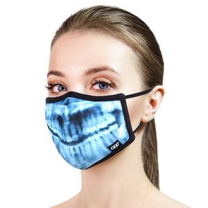 The image shows a young woman wearing a blue and black face mask with an x-ray of teeth on it. The mask has black ear loops and a black border around the edge. The woman has light skin, brown hair, and blue eyes. She is looking at the camera with a neutral expression.