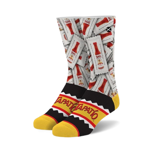 A pair of crew socks showcasing a repeating pattern of Tapatio hot sauce packets on a white background. The cuff features a black and yellow Tapatio logo.