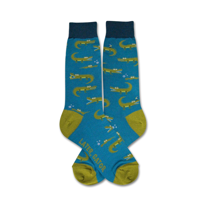 Pair of teal crew socks with a pattern of smiling green alligators and bubbles.  The socks have olive green heels and toes. }}