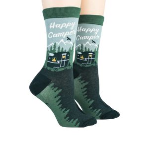 A pair of green crew socks with a pattern of happy camper text, mountains, and a camper.