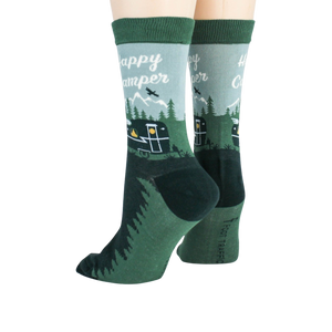 A pair of green crew socks with a pattern of happy camper text, mountains, and a camper.