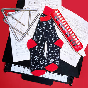 Flat lay of 'Dancing Notes' socks on sheet music with musical instruments, creating a musical setting.