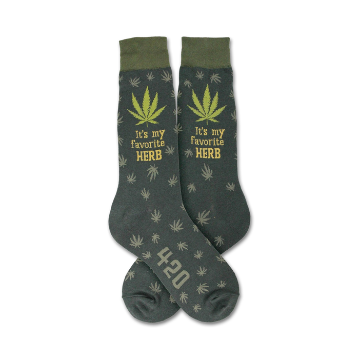 Pair of dark-green crew socks with a repeating cannabis leaf pattern, 'It's my favorite HERB' text, and '420' detail.