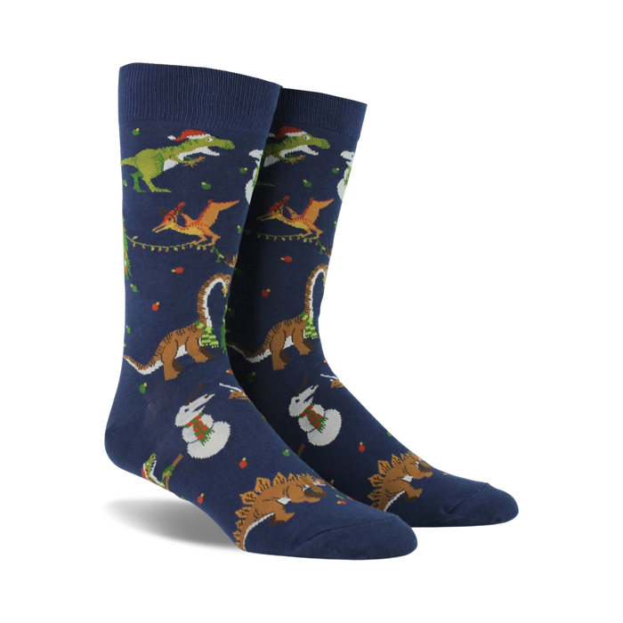 Pair of navy blue crew socks. Feature a whimsical Christmas design with dinosaurs decorating trees and snowmen.