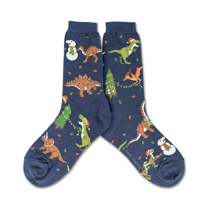 A pair of navy blue crew socks showcasing a whimsical Christmas design. The socks feature various dinosaurs wearing Santa hats and celebrating around decorated Christmas trees and snowmen. }}