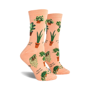 A pair of peach-colored crew socks with a fun pattern of potted plants and plant puns like 'Never leaf me'.