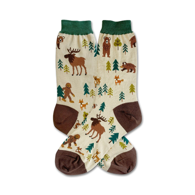 Cream crew socks with brown and green accents. Design features illustrated woodland creatures like moose, bears, Bigfoot, and foxes among stylized evergreen trees.