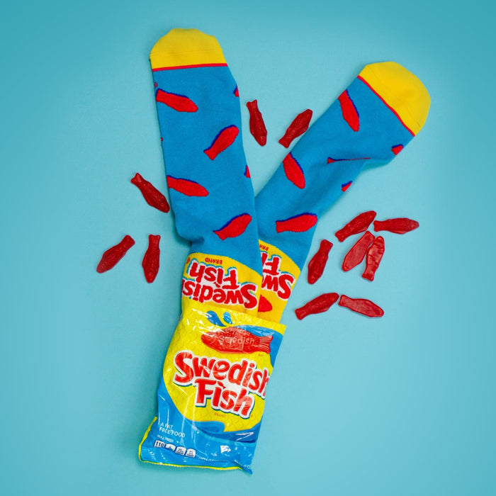 Flatlay product shot of Swedish Fish socks and a bag of Swedish Fish candy on a light blue background.