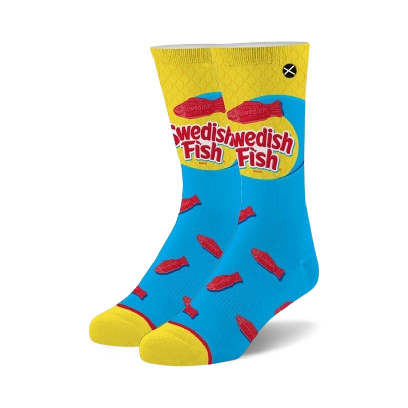 Pair of crew socks in blue with yellow cuffs. The socks feature a repeated pattern of red Swedish Fish candies and the Swedish Fish logo.