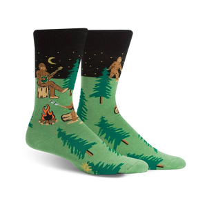 Pair of green and black crew socks featuring a whimsical Sasquatch playing banjo around a campfire in the woods.