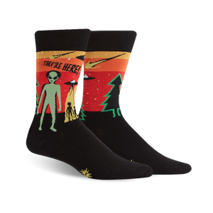 Black crew socks with a retro alien abduction scene in orange, green, and red. The text 'They're Here!' is featured.