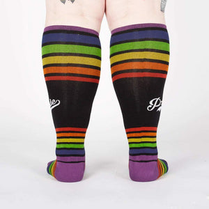 A pair of black knee-high socks with a wide purple cuff and alternating thin and wide rainbow stripes. The word 