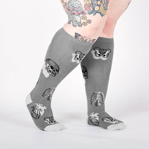 Lifestyle shot showing a model wearing the anatomical knee-high socks.  The socks are gray with skulls, ribcages, and hearts.