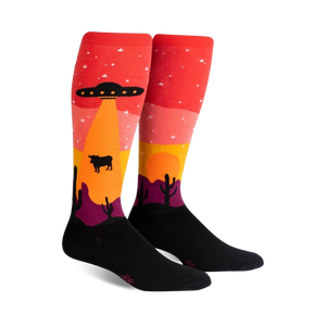 Pair of knee-high socks; red, orange, yellow, purple, and black. Design features an alien spaceship abducting a cow in a desert landscape at sunset.
