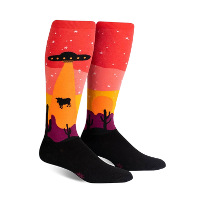 Pair of knee-high socks; red, orange, yellow, purple, and black. Design features an alien spaceship abducting a cow in a desert landscape at sunset.