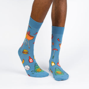 A pair of blue socks with a pattern of cartoon hot dogs, steaks, and grilling accessories.
