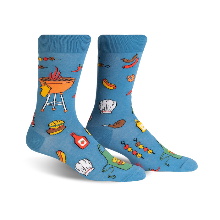 A pair of light blue crew socks with a fun BBQ design featuring burgers, hot dogs, grilling equipment, and chef hats.