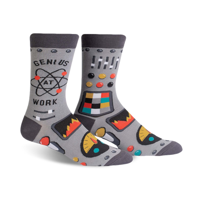 Pair of gray crew socks with a robot control panel design, atom graphic, and the phrase 'Genius at Work'. Features pops of orange, teal, and yellow.