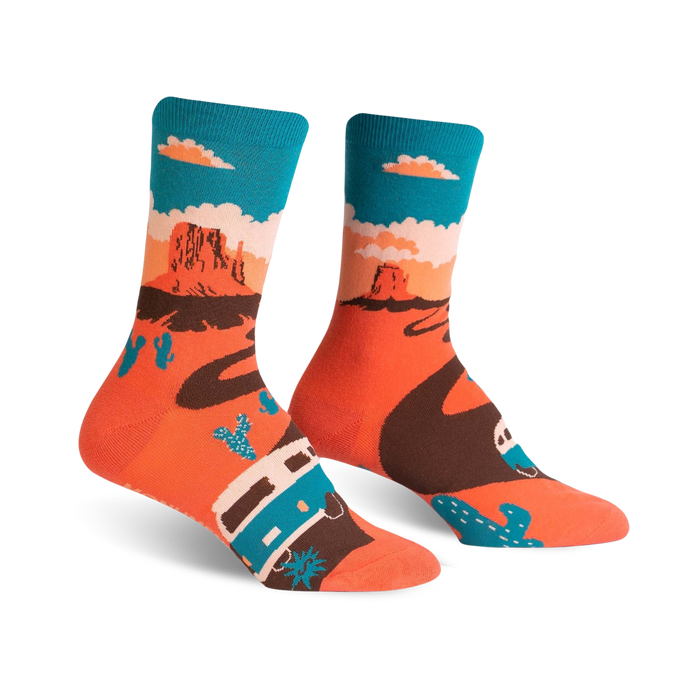 A pair of crew socks with a Monument Valley theme. The socks are coral orange with a brown winding road, teal camper van, and cacti against a teal sky. }}