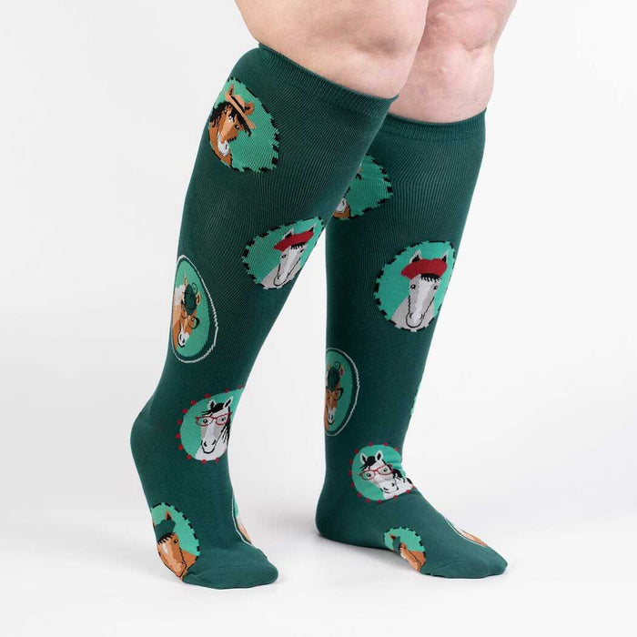 A pair of green knee-high socks with a pattern of cartoon horses wearing glasses on them.
