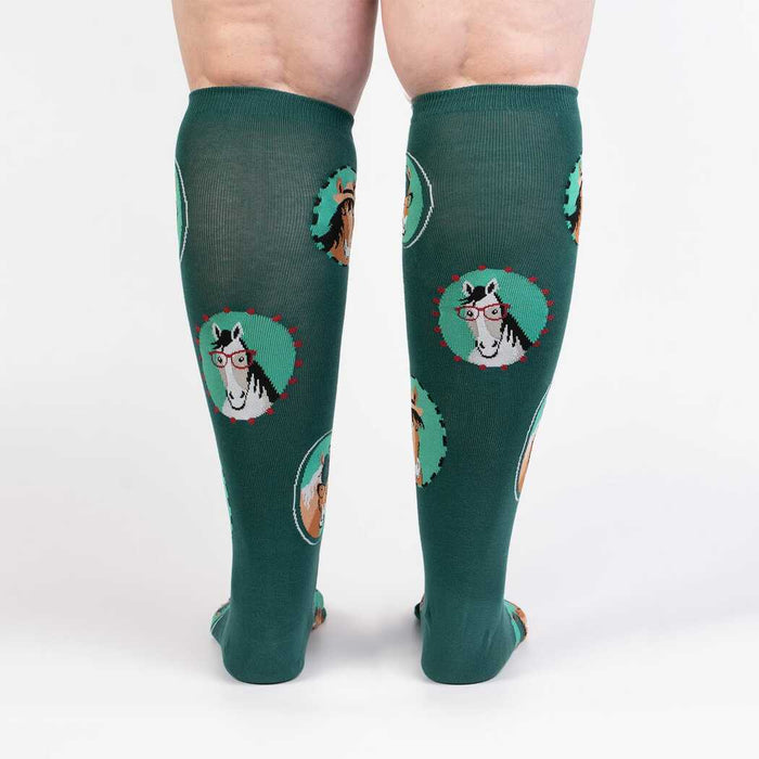 A pair of green knee-high socks with a pattern of cartoon horses wearing glasses on them.