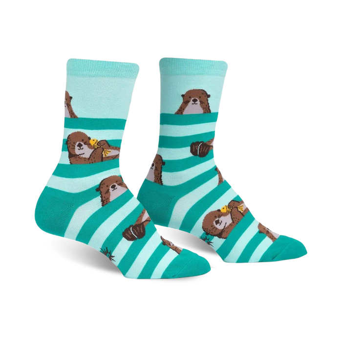 Crew socks in teal and mint green stripes featuring adorable otter designs. Otters are shown peeking from behind the stripes.