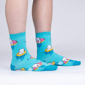 Lifestyle shot showing the socks on a person's feet; teal crew socks with white cats on donut floats.