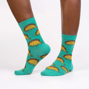 A pair of green socks with a pattern of tacosaurus, a dinosaur with a taco shell for a body.