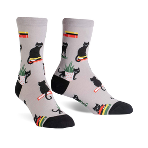 Pair of grey crew socks with a repeating pattern of black cats sitting on books and in potted plants.  Red, yellow, and green accents.