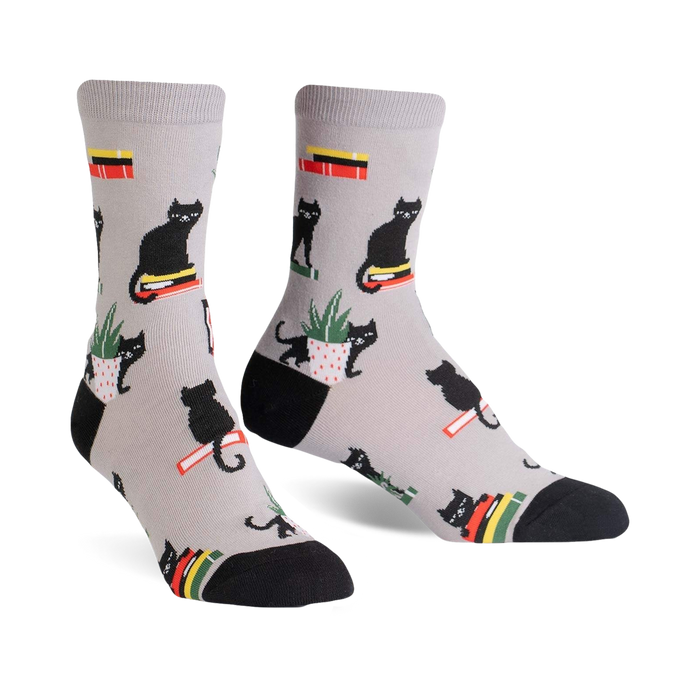 Pair of grey crew socks with a repeating pattern of black cats sitting on books and in potted plants.  Red, yellow, and green accents.