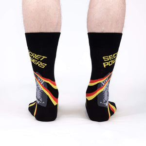 A pair of black socks with a colorful pattern of red, yellow, and white stripes and a picture of the character He-Man. The socks have the text 
