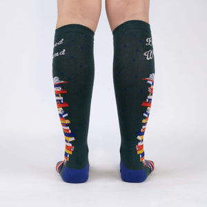 A pair of green knee-high socks with a pattern of books on them. The socks have the words 