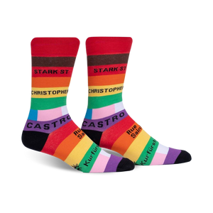 A pair of crew socks in red, orange, yellow, green, blue, purple, and black.  The socks feature rainbow stripes and street names in black text.