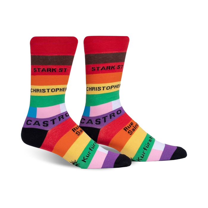 A pair of crew socks in red, orange, yellow, green, blue, purple, and black.  The socks feature rainbow stripes and street names in black text.