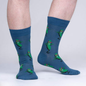 Lifestyle shot of model wearing a pair of blue crew socks with a fun pickle pattern.