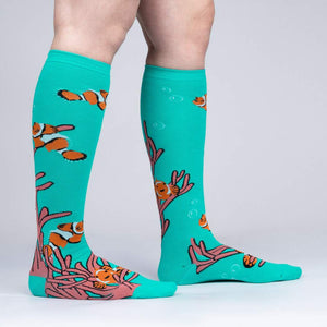 A pair of knee-high socks with an all-over pattern of orange clownfish and pink coral on an aqua background.
