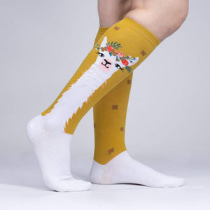 A pair of yellow and white knee-high socks with a llama face on the back of each sock.