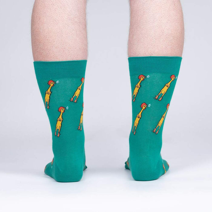 A pair of green socks with a pattern of cartoon chickens wearing party hats and blowing noisemakers.
