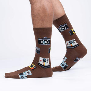 Lifestyle shot showing brown camera socks on a person's legs against a white background.