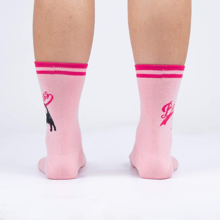 Rear view of a person's legs wearing pink 'Bad Ass Cat' socks, showing the full design on the back of the socks.