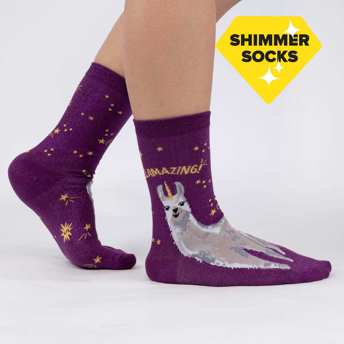 A pair of purple socks with a llama wearing a gold crown on each sock. The socks have the words 