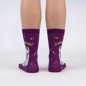 A pair of purple socks with a llama wearing a gold crown on each sock. The socks have the words 