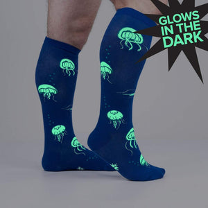 Close-up showing the 'Nice to Sea You' socks glowing in the dark, emphasizing the neon green jellyfish against the blue background.