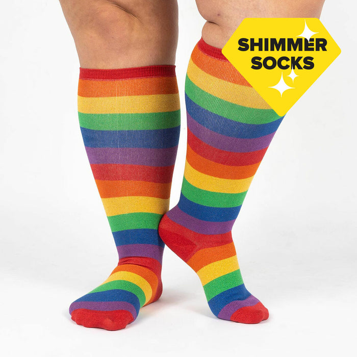 A pair of knee-high socks with red toes and heels and a rainbow of colors in between. The socks are being modeled by a person with large calves.
